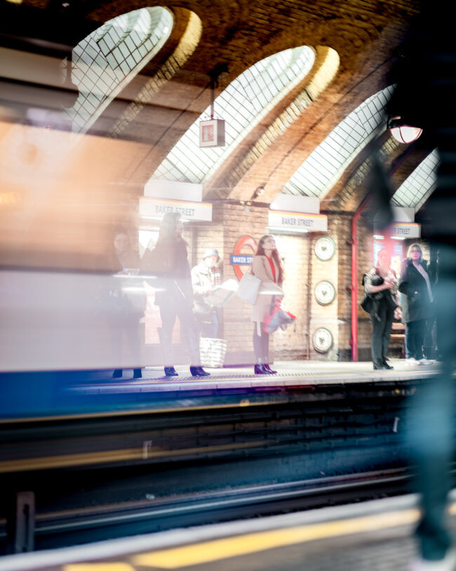 Fotografia Lunga Esposizione alla Stazione Metro di Baker Street, Londra: Incrocio di Persone a Fuoco e Treno in Movimento Sfuocato