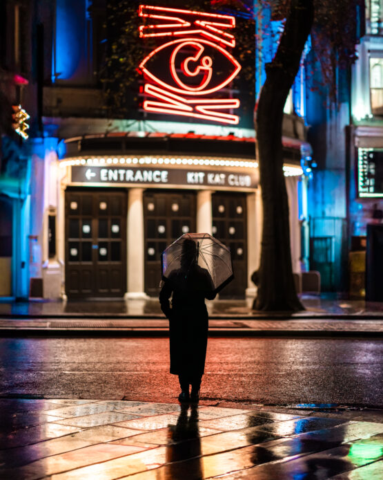 Ragazza con Ombrello Trasparente di Fronte a un Locale, Giochi di Luci Scintillanti Dopo la Pioggia, Un'Atmosfera Unica Catturata nelle Strade di Londra.
