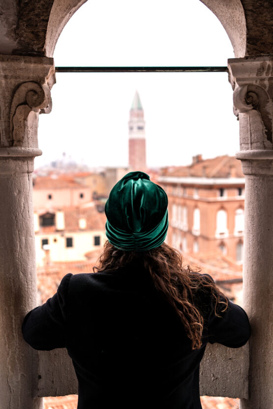 Ragazza girata di spalle con un turbante verde smeraldo affacciata dalla scala canterini del bovolo ammirando il campanile di piazza san marco