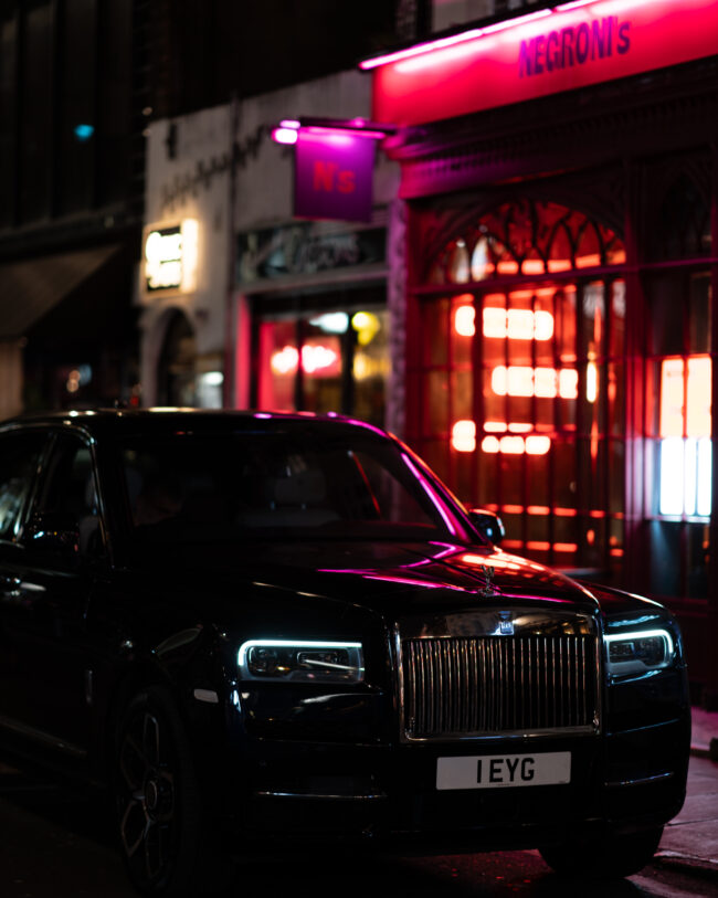 Fotografia Notturna a Londra: Rolls Royce Illuminata davanti a Locale con Insegne Vibranti tra Violaceo e Rosso Intenso