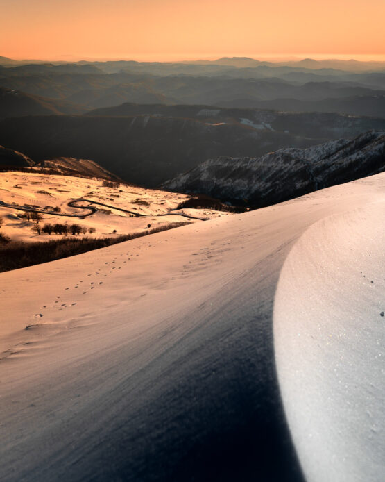 Magico Tramonto in Montagna durante una Giornata Nevosa: Colori Incredibili, Dune di Neve e Strade a Tornanti, un'Immagine Catturata con lo Splendore della Natura.