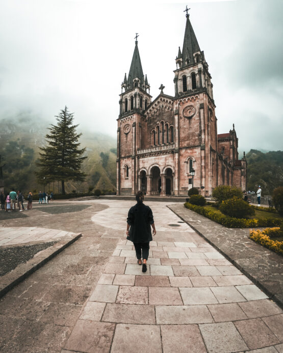 Santuario di Covadonga: Atmosfera Sacra con una Ragazza al Centro che Cammina Verso l'Ingresso, Esplorando la Bellezza Architettonica.