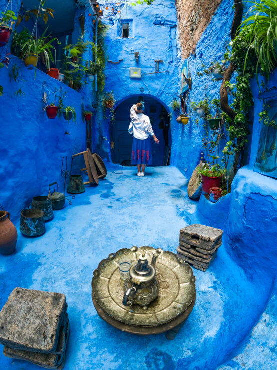 Fotografia a Chefchaouen, Marocco: ragazza Che Osserva una Porta all'Interno di un'Abitazione Completamente Colorata di Azzurro.