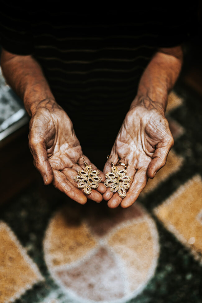 Dettaglio in Primo Piano di mani della Signora Marchigiana che Lavora con il Tombolo, Tenendo tra le mani con orgoglio Due Orecchini da Lei Creati con Maestria.