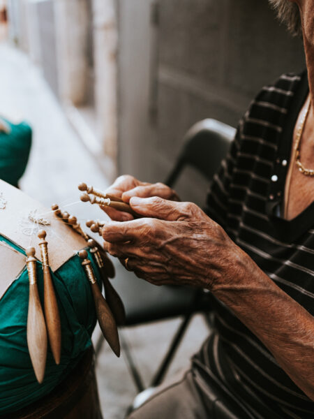 "Mani Esperte al Tombolo nelle Marche: Dettaglio in Primo Piano di una Signora che Lavora con Abilità e Passione nell'Antica Arte del Tombolo."