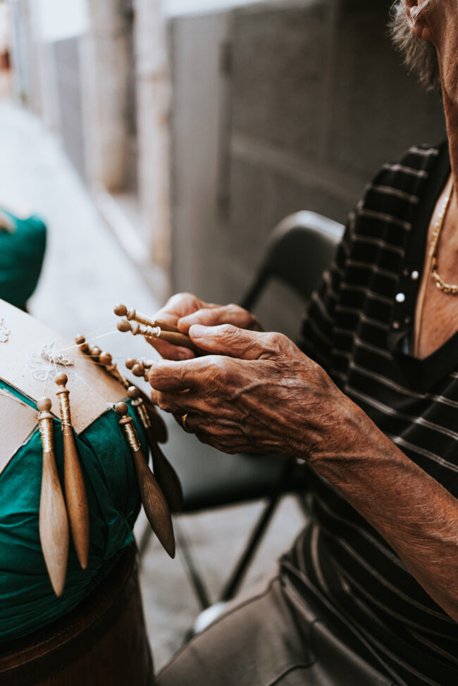 "Mani Esperte al Tombolo nelle Marche: Dettaglio in Primo Piano di una Signora che Lavora con Abilità e Passione nell'Antica Arte del Tombolo."