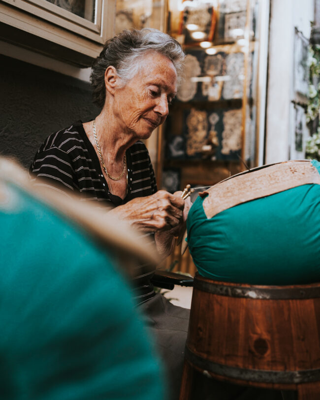 "Mani Esperte al Tombolo nelle Marche: Ritratto di una Signora che Lavora con Abilità e Passione nell'Antica Arte del Tombolo."