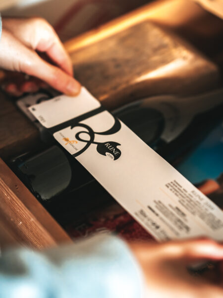 Precisione Artigianale: Mani che Attaccano un'Etichetta a una Bottiglia di Vino, un Momento Cruciale nel Processo di Imbottigliamento.