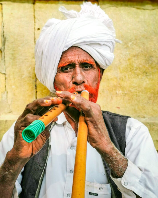 Ritratto di santone indiano con turbante bianco, sopracciglia e barba arancione, mentre suona un flauto.