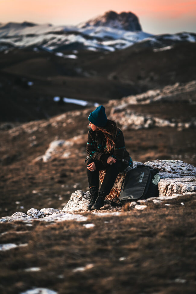 Ragazza seduta di profilo su una pietra di montagna bianca, accanto a una borsa del brand GoPro, con uno sfondo mozzafiato di montagne innevate.