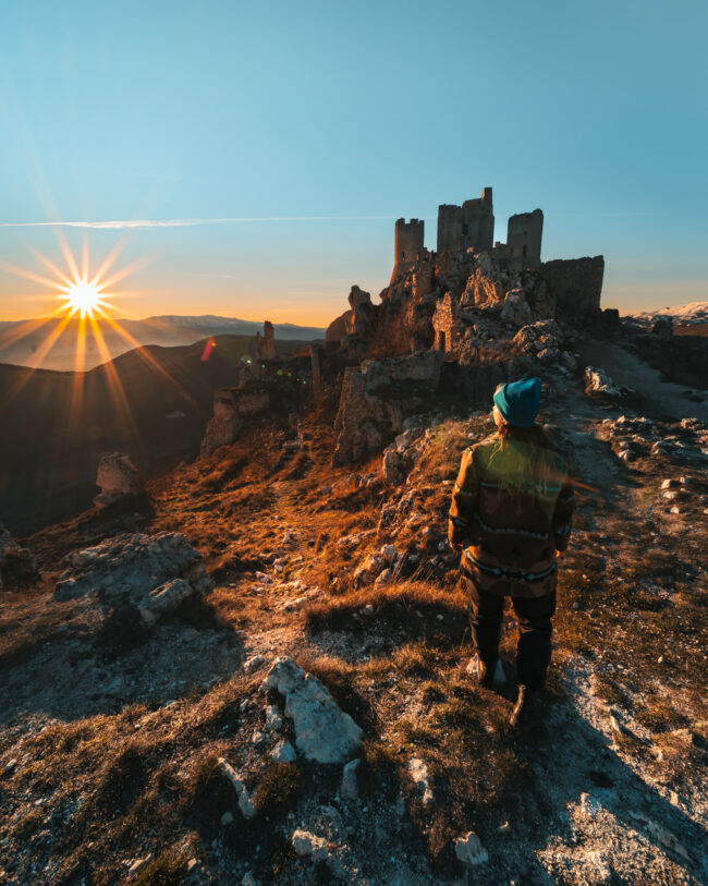 Ragazza al tramonto posa con eleganza di fronte a Rocca Calascio, promuovendo un brand d'abbigliamento.