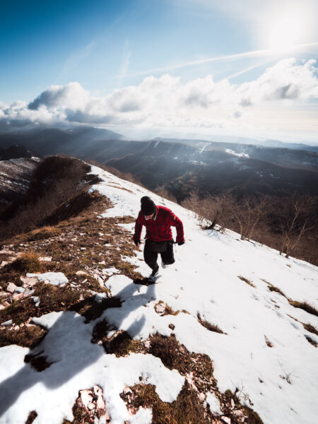 Ragazzo che cammina in salita lungo la cresta di una montagna innevata, indossando abbigliamento invernale sotto un cielo incredibile.
